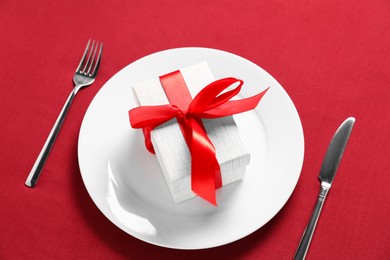 Photo of Gift and setting for romantic dinner on red background, closeup