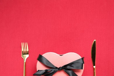 Heart shaped romantic gift and cutlery on red background, top view. Space for text