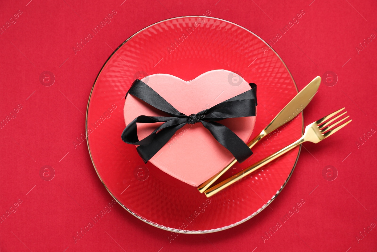 Photo of Heart shaped gift and setting for romantic dinner on red background, top view