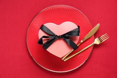 Heart shaped gift and setting for romantic dinner on red background, top view