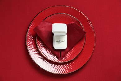 Beautiful engagement ring and setting for romantic dinner on red background, top view