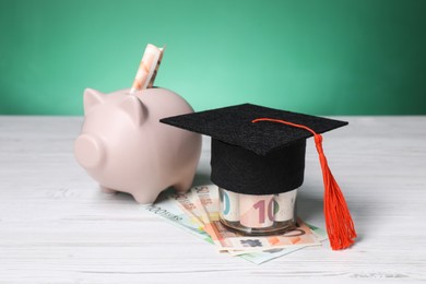 Photo of Graduate hat, euro banknotes and piggy bank on light wooden table. Tuition payment