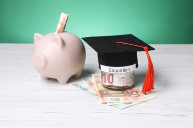 Photo of Graduate hat, euro banknotes, piggy bank and glass jar with word Education on light wooden table. Tuition payment