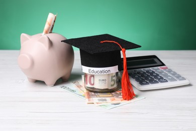 Photo of Graduate hat, euro banknotes, piggy bank, calculator and glass jar with word Education on light wooden table. Tuition payment