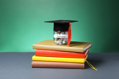 Photo of Graduate hat, dollar banknotes in glass jar with word Education and books on grey table. Tuition payment