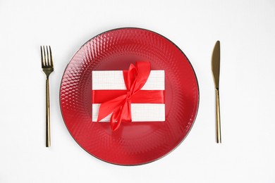 Photo of Gift box, plate and cutlery on white table, flat lay. Beautiful table setting for romantic dinner