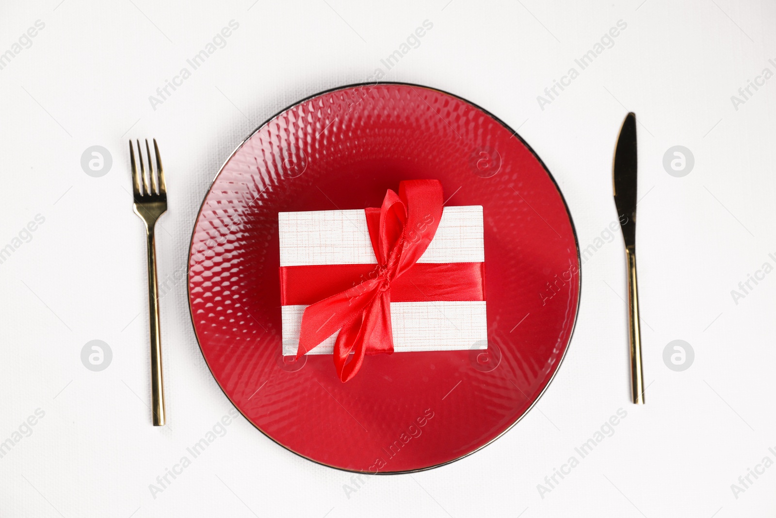 Photo of Gift box, plate and cutlery on white table, flat lay. Beautiful table setting for romantic dinner