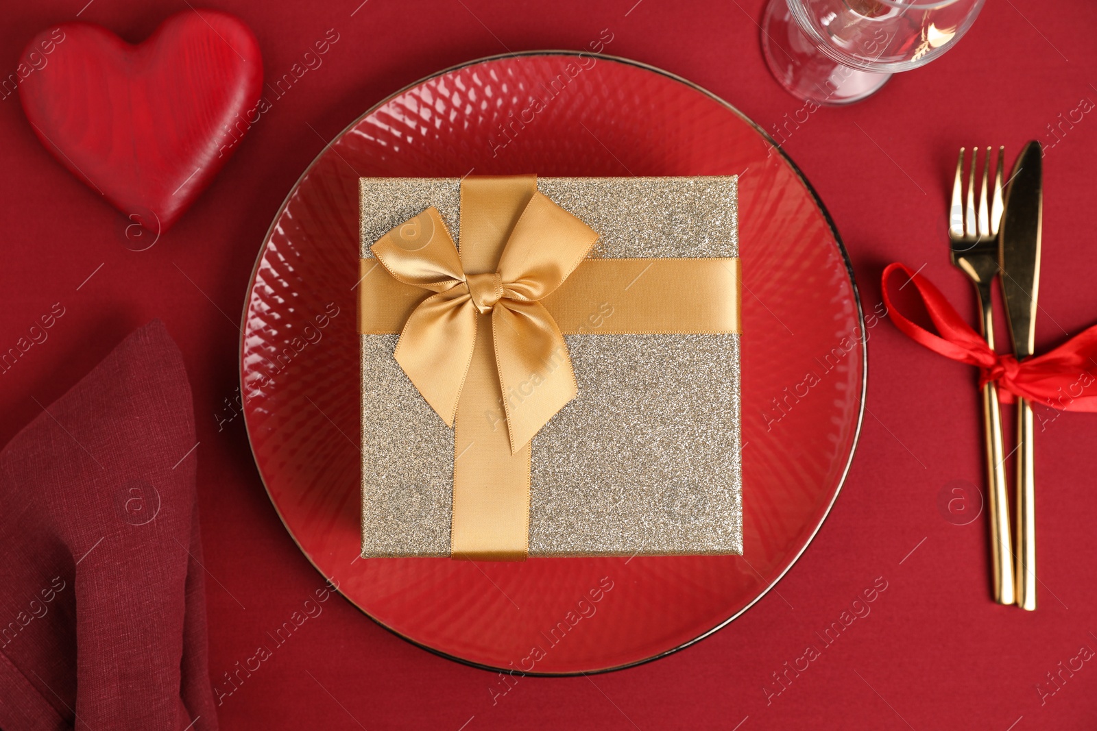 Photo of Gift box and tableware on red table, flat lay. Table setting for romantic Valentine's day celebration