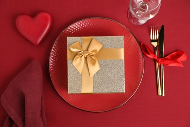 Photo of Gift box and tableware on red table, flat lay. Table setting for romantic Valentine's day celebration