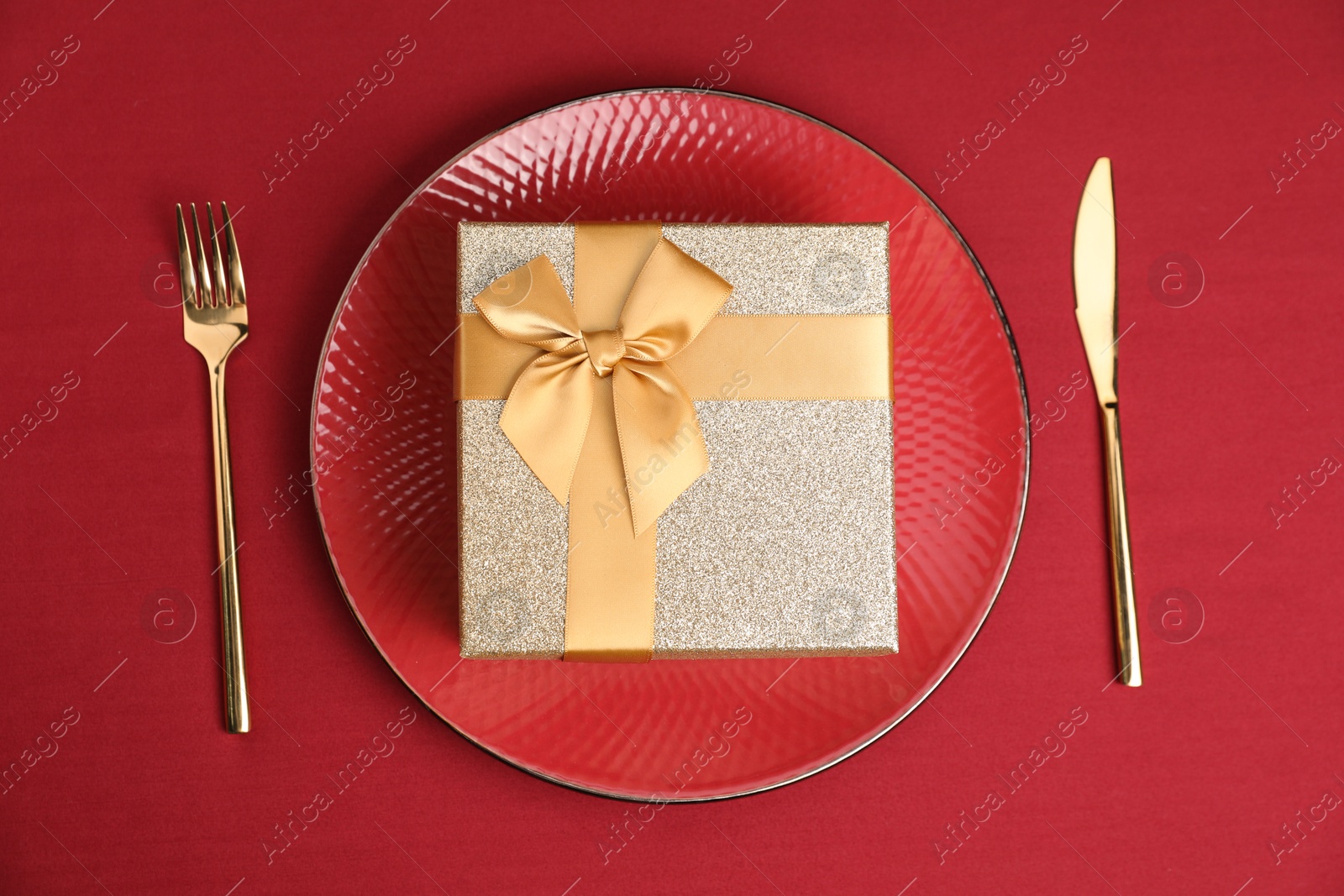 Photo of Gift box and tableware on red table, flat lay. Table setting for romantic dinner