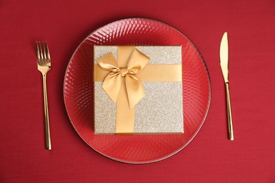 Gift box and tableware on red table, flat lay. Table setting for romantic dinner