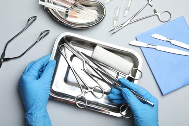 Doctor with different surgical tools on gray background, top view