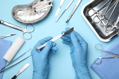 Doctor with different surgical tools on light blue background, top view