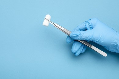 Photo of Doctor holding surgical tweezers with gauze on light blue background, closeup. Space for text