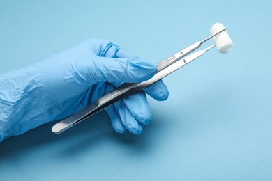 Photo of Doctor holding surgical tweezers with gauze on light blue background, closeup