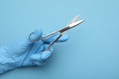 Photo of Doctor with surgical scissors on light blue background, closeup. Space for text