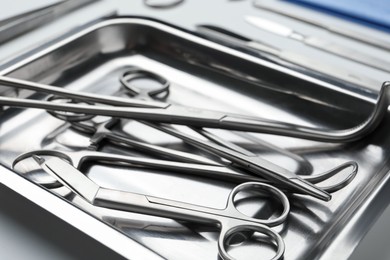 Photo of Different surgical tools in metal tray on light background, closeup