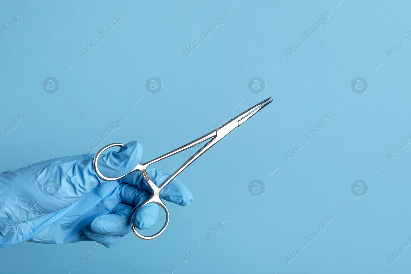 Photo of Doctor with surgical forceps on light blue background, closeup. Space for text