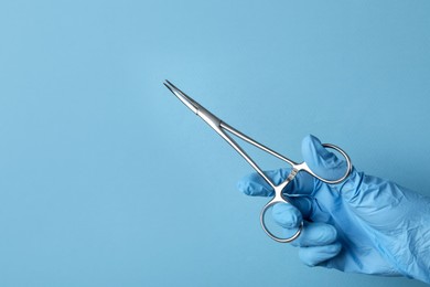 Photo of Doctor with surgical forceps on light blue background, closeup. Space for text