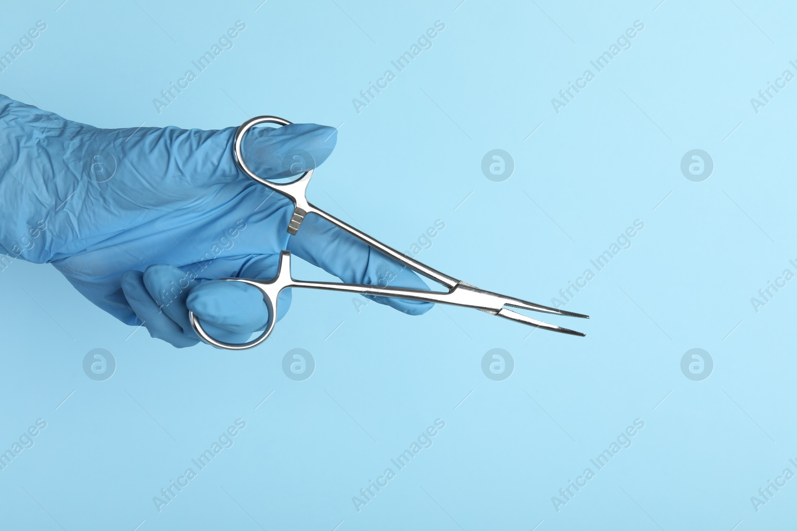 Photo of Doctor with surgical forceps on light blue background, closeup. Space for text