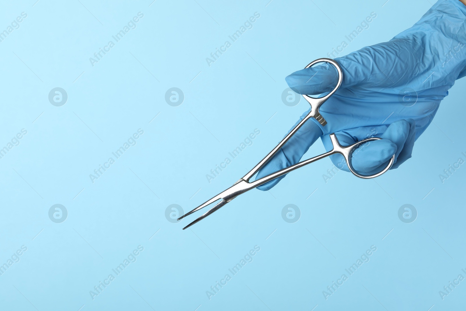 Photo of Doctor with surgical forceps on light blue background, closeup. Space for text