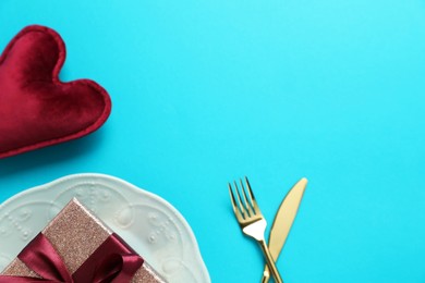 Beautiful table setting with romantic gift and heart on light blue background, flat lay. Space for text