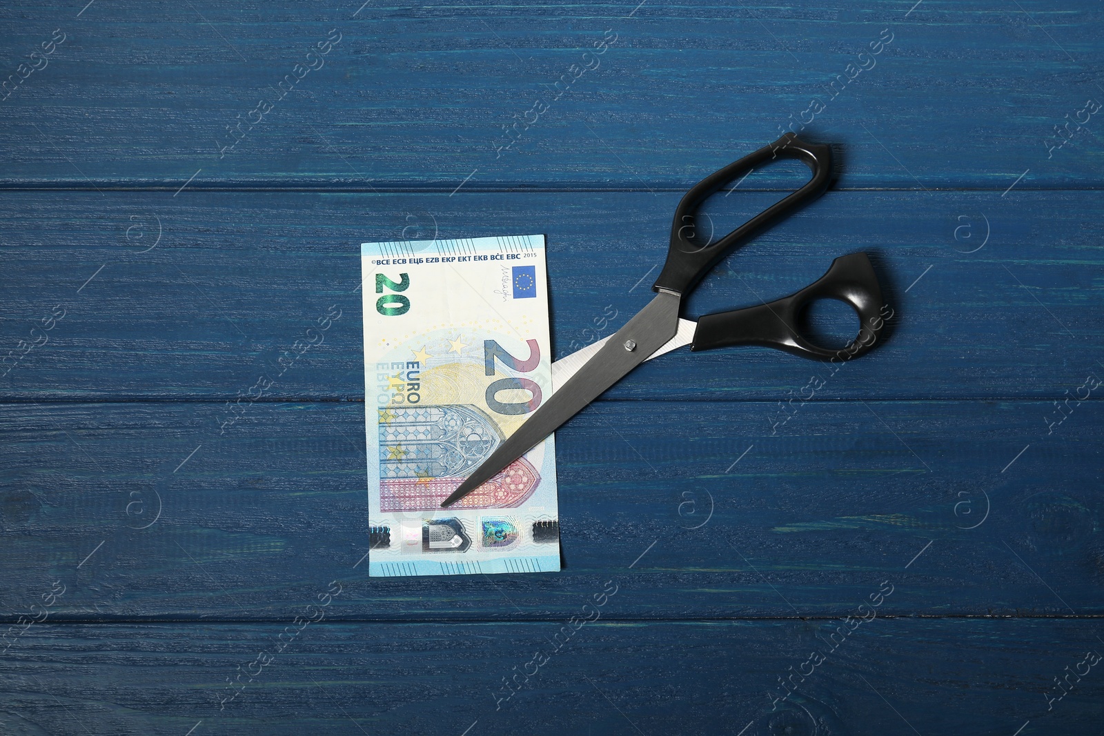 Photo of Scissors with euro banknote on blue wooden table, top view