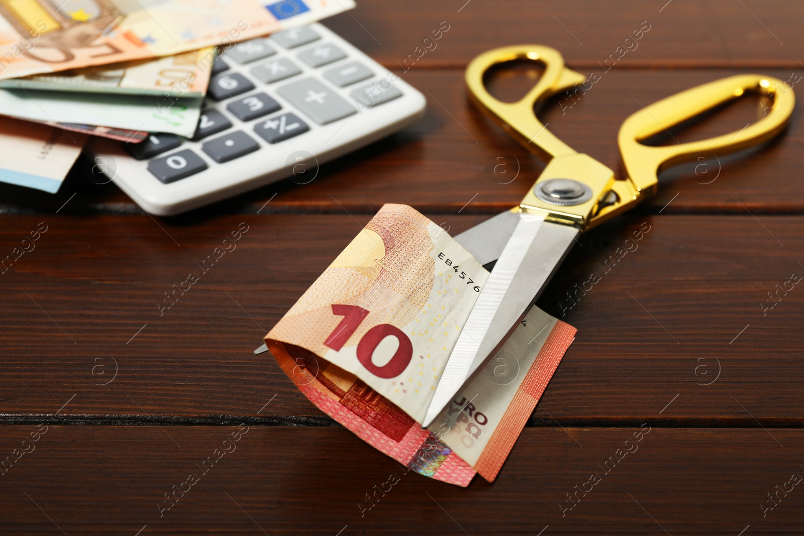 Photo of Euro banknotes, scissors and calculator on wooden table, closeup