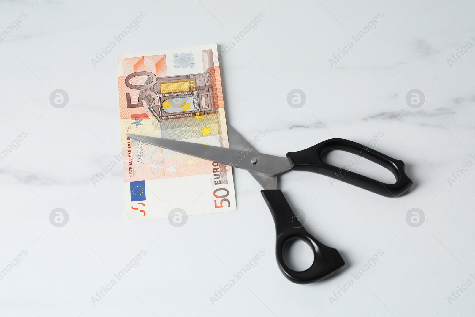 Photo of Scissors with euro banknote on light marble table, above view