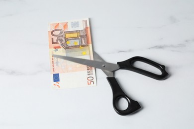 Photo of Scissors with euro banknote on light marble table, above view