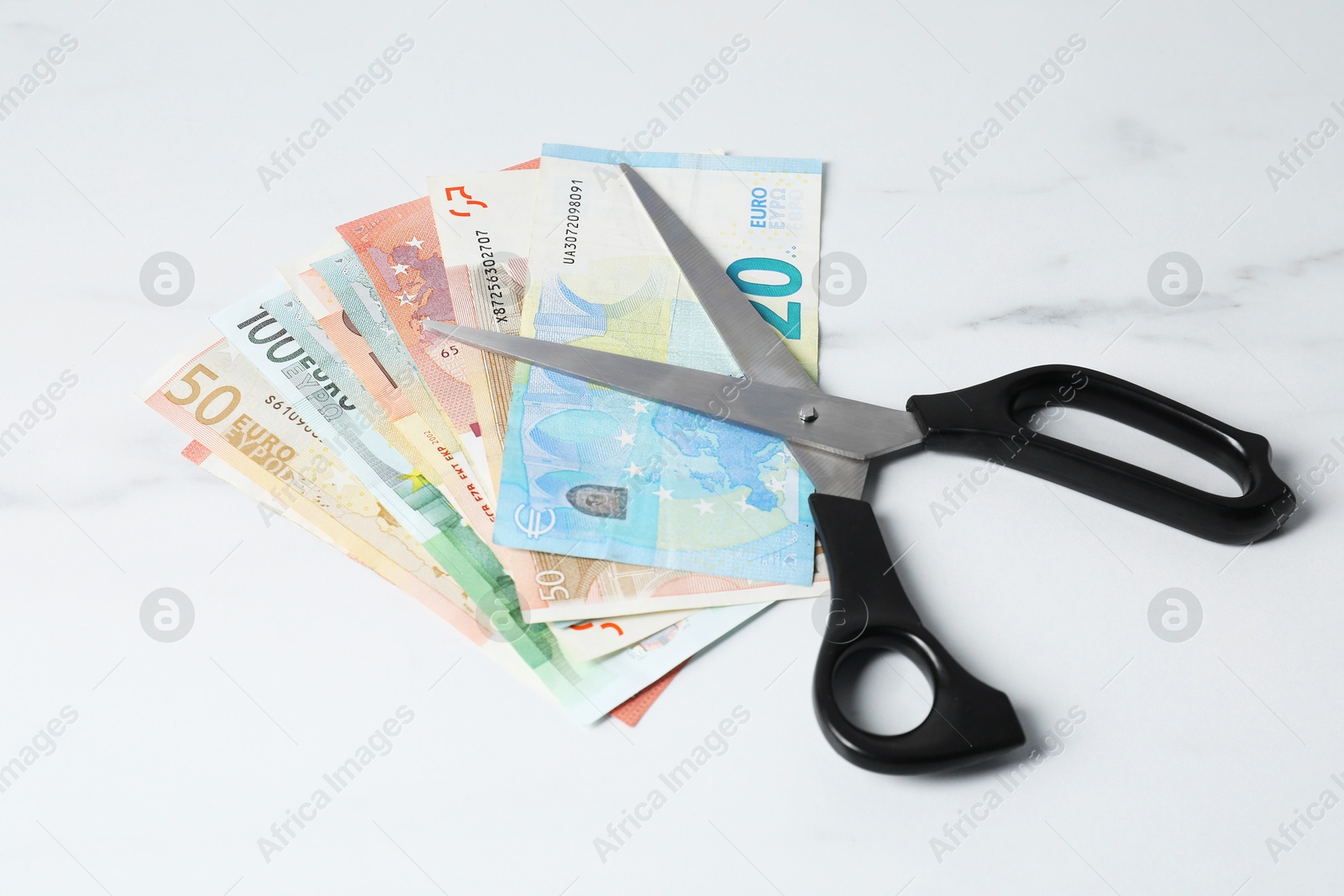 Photo of Euro banknotes and scissors on light marble table