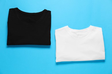 Photo of Blank t-shirts for branding on light blue background, flat lay. Mockup for design