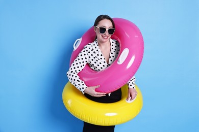 Photo of Businesswoman with inflatable rings and sunglasses on light blue background