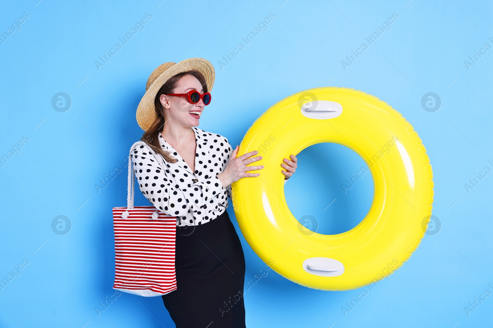 Photo of Businesswoman with inflatable ring, straw hat, bag and sunglasses on light blue background