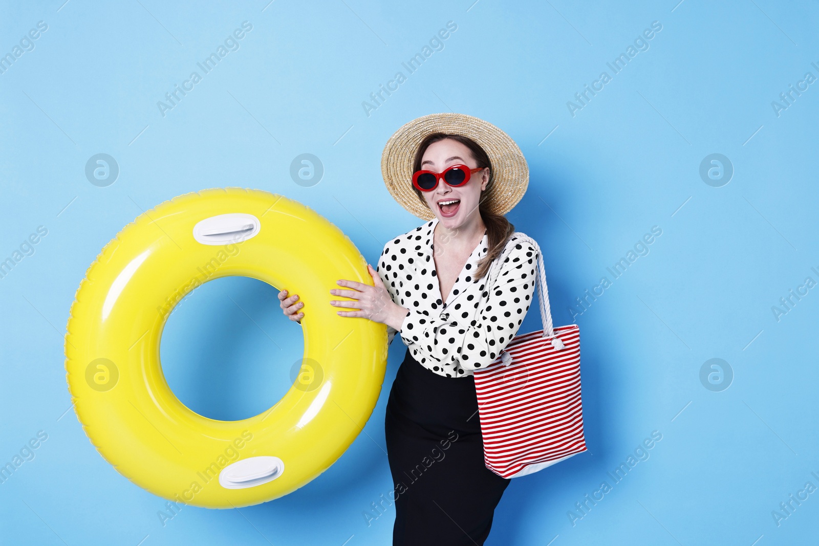 Photo of Businesswoman with inflatable ring, straw hat, bag and sunglasses on light blue background