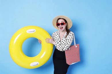 Businesswoman with inflatable ring, straw hat, bag and sunglasses on light blue background