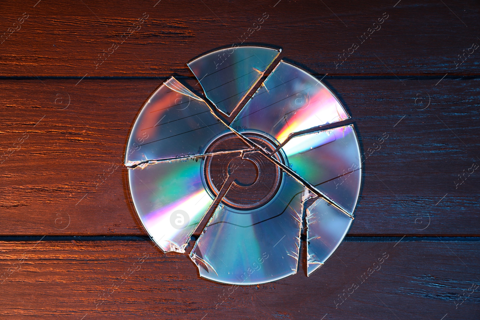 Photo of Broken compact disc on wooden background, top view