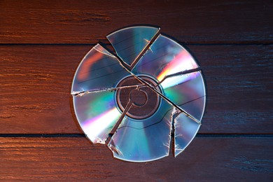 Photo of Broken compact disc on wooden background, top view