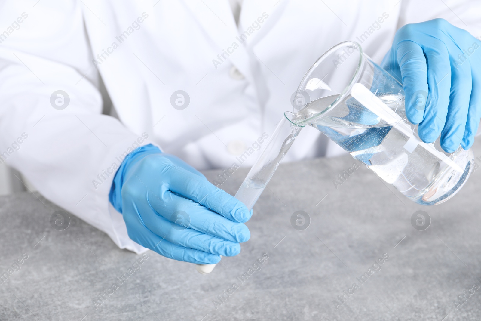 Photo of Laboratory testing. Scientist pouring liquid into test tube at grey table indoors, closeup