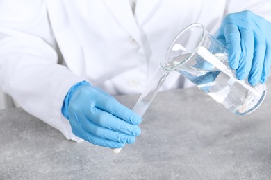 Photo of Laboratory testing. Scientist pouring liquid into test tube at grey table indoors, closeup