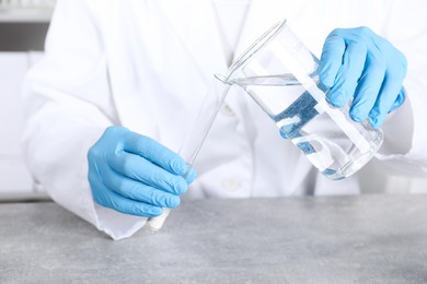 Photo of Laboratory testing. Scientist pouring liquid into test tube at grey table indoors, closeup