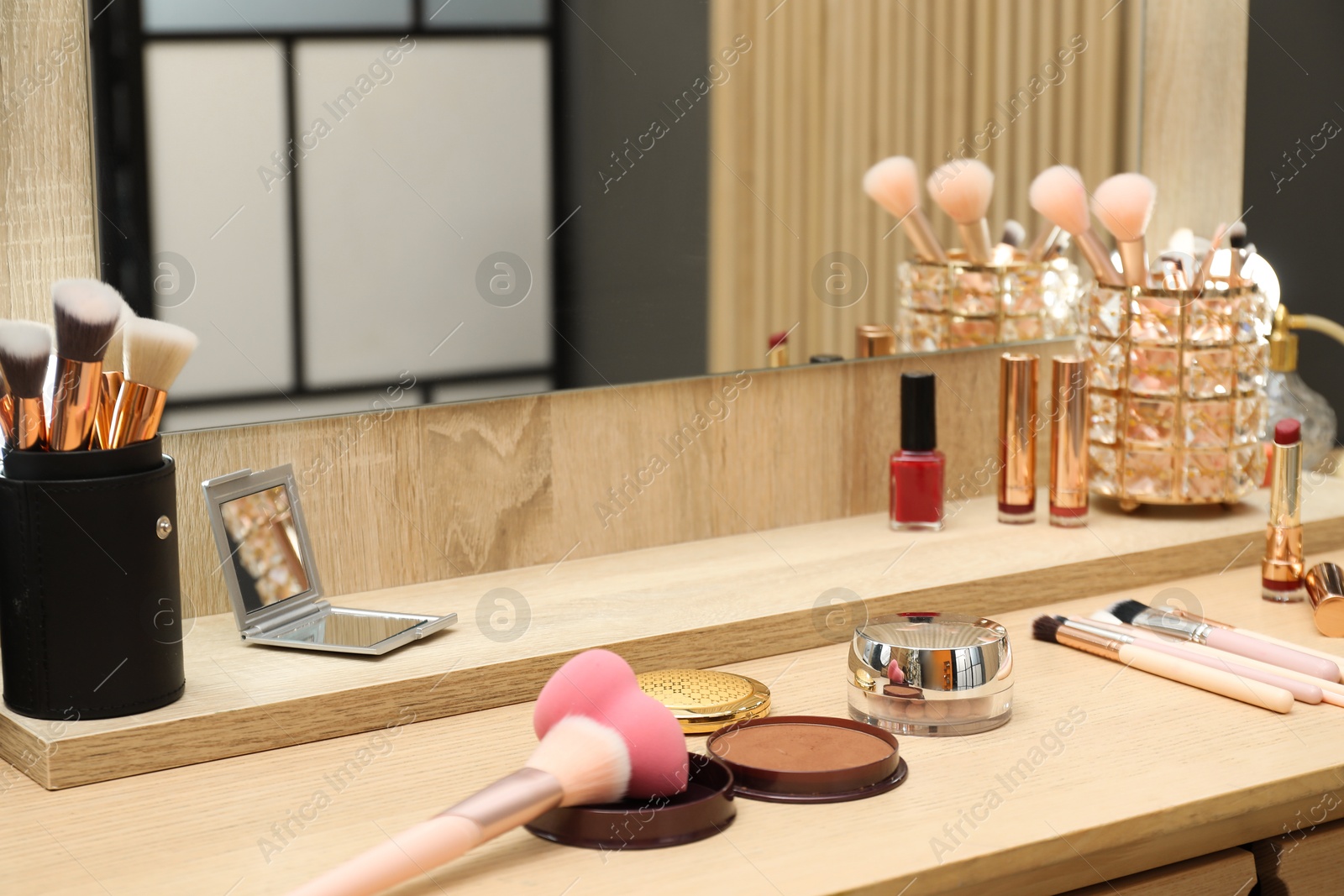 Photo of Makeup room. Wooden dressing table with mirror and different beauty products indoors, closeup