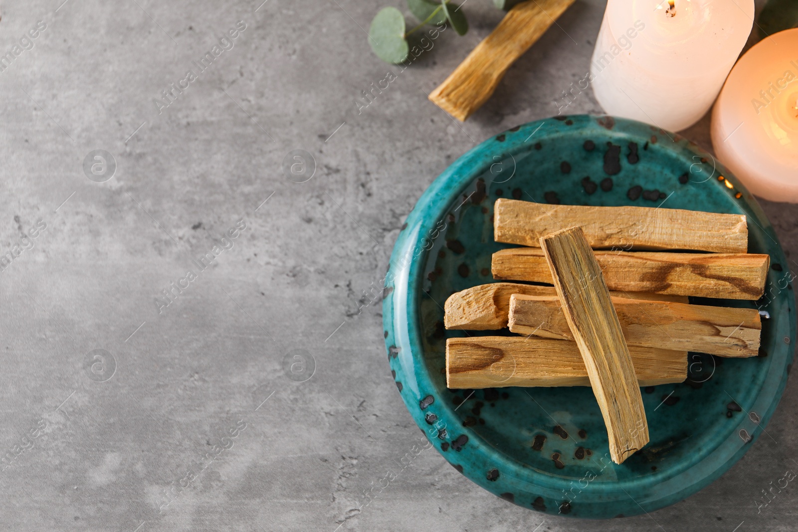 Photo of Palo santo sticks and burning candles on grey table, flat lay. Space for text