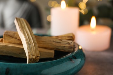 Photo of Palo santo sticks and burning candles on table, closeup