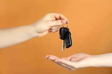 Photo of Saleswoman giving car key to customer on orange background, closeup. Buying auto