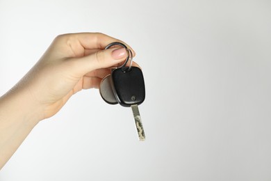 Photo of Woman with car key and keychain on light grey background, closeup. Space for text