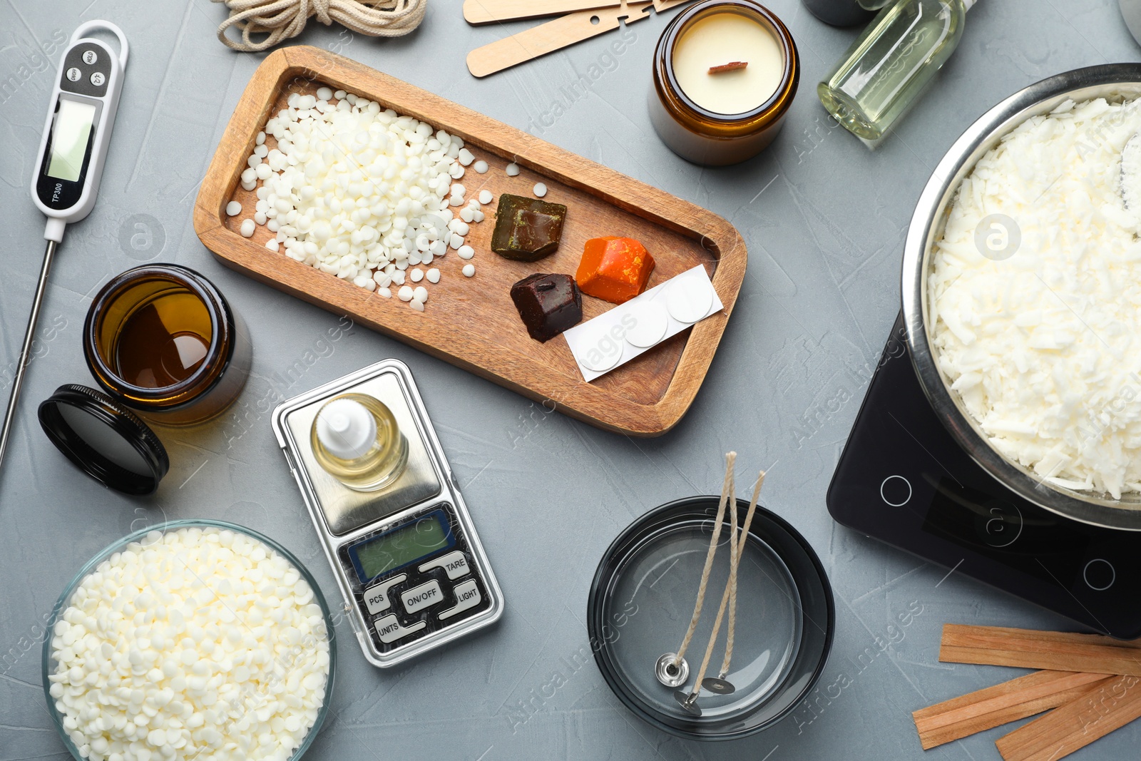 Photo of Soy wax, essential oil and different tools for making candles on gray textured table, flat lay