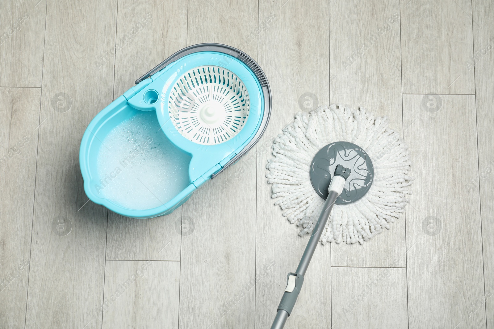 Photo of String mop and bucket with detergent on wooden floor, top view