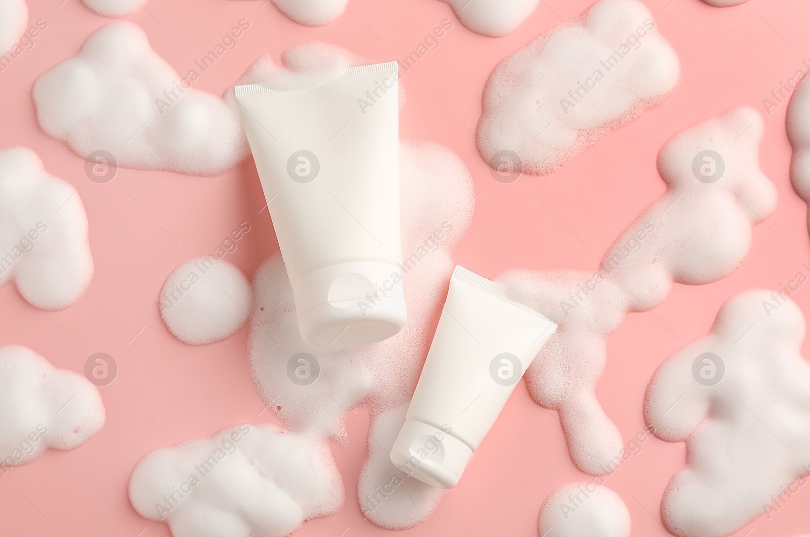 Photo of Tubes of cosmetic products with foam on pink background, top view