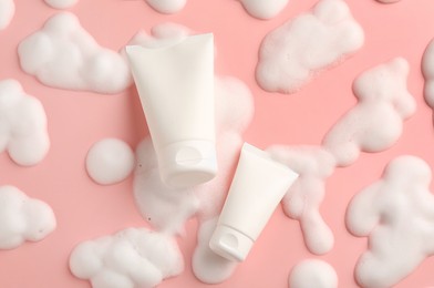 Tubes of cosmetic products with foam on pink background, top view